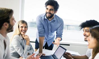 Fünf junge Menschen in einem modernen Büro in lebhafter Diskussion, lachend und mit Laptop – symbolisiert innovative Zusammenarbeit im Bereich Digitalisierung und Management.