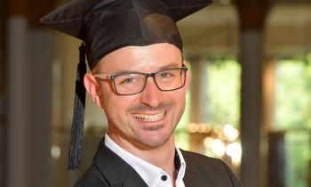 Arno Kersche mit Abschlusskappe und Brille, lachend in festlicher Umgebung – Symbol für seinen erfolgreichen MBA-Abschluss an der FH Burgenland.