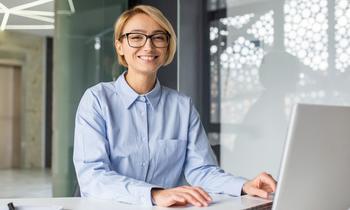Junge Frau mit Brille sitzt freundlich lächelnd an einem Schreibtisch mit Laptop – Symbolbild für das berufsbegleitende MBA-Programm in Compliance, ESG und Risikomanagement an der Hochschule Burgenland.