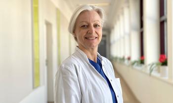 Birgit Giese im weißen Kittel lächelt in einem hellen Klinikflur in die Kamera.