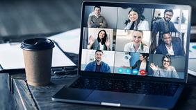 Laptop auf einem Tisch zeigt ein virtuelles Meeting mit mehreren lächelnden Teilnehmer*innen; im Vordergrund steht ein Kaffeebecher – symbolisiert digitale Vernetzung beim Online Welcome Event.