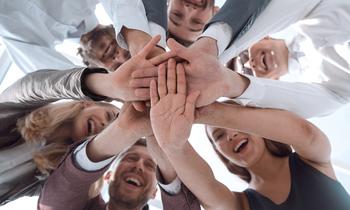 Teamgeist und Zusammenhalt an der Hochschule Burgenland Weiterbildung GmbH Eine Gruppe von Menschen steht im Kreis und legt die Hände übereinander, um Zusammenhalt und Teamgeist zu zeigen
