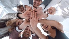 Teamgeist und Zusammenhalt an der Hochschule Burgenland Weiterbildung GmbH Eine Gruppe von Menschen steht im Kreis und legt die Hände übereinander, um Zusammenhalt und Teamgeist zu zeigen