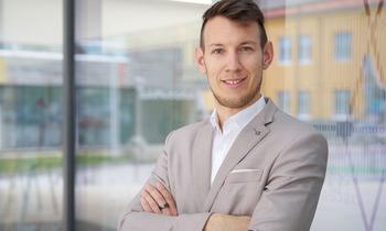 Porträt von Christoph Tatzber im Anzug, aufgenommen im Freien. Im Hintergrund ist ein helles Gebäude erkennbar – Symbolbild für beruflichen Erfolg und persönliche Weiterentwicklung.
