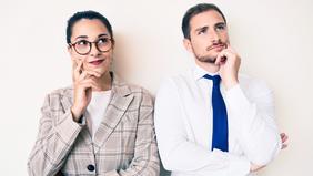 Nachdenklich blickende Frau mit Brille und Mann im Business-Outfit stehen nebeneinander vor hellem Hintergrund – Symbolbild für rechtliche Fragen und gesetzliche Änderungen.