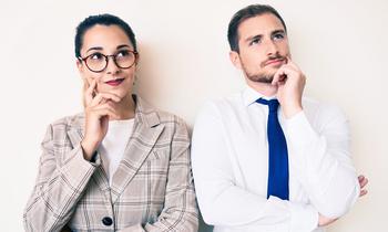 Nachdenklich blickende Frau mit Brille und Mann im Business-Outfit stehen nebeneinander vor hellem Hintergrund – Symbolbild für rechtliche Fragen und gesetzliche Änderungen.