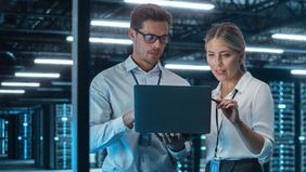Diploma of Advanced Studies in Informationssicherheit und IT-Risikomanagement Zwei IT-Fachkräfte in einem modernen Serverraum analysieren gemeinsam Daten auf einem Laptop – Symbolbild für Informationssicherheit und IT-Risikomanagement im Rahmen des neuen Weiterbildungsprogramms der FH Burgenland.