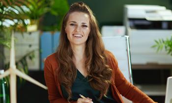 Junge Frau mit langen Haaren sitzt in einem modernen Büro, lächelt freundlich in die Kamera – Symbolbild für das MBA-Studium Energiewirtschaft an der Hochschule Burgenland.