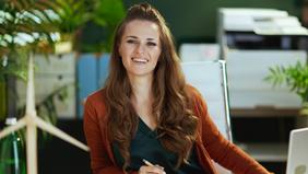 Junge Frau mit langen Haaren sitzt in einem modernen Büro, lächelt freundlich in die Kamera – Symbolbild für das MBA-Studium Energiewirtschaft an der Hochschule Burgenland.