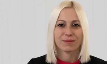 Porträt von Manuela Schoyswohl, MBA-Absolventin der FH Burgenland, mit blondem Haar, schwarzem Blazer und rotem Shirt, vor hellem Hintergrund.