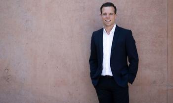 Patrick Söndgen, MBA-Alumnus der FH Burgenland, steht lässig im dunklen Anzug vor einer Betonwand und lächelt in die Kamera.