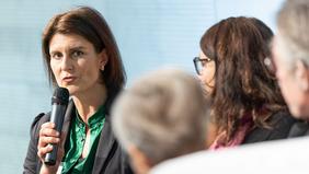 Bettina Schauer-Frank, Lehrgangsleitung AIM, spricht bei einer Podiumsdiskussion im Rahmen der AQ Austria Jahrestagung 2022 in Wien in ein Mikrofon, flankiert von weiteren Teilnehmerinnen.