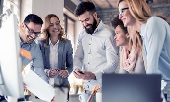 Engagiertes Team in moderner Arbeitsumgebung schaut gemeinsam auf einen Bildschirm – steht sinnbildlich für kollaboratives, praxisnahes Lernen im MBA E-Commerce und Online-Marketing der FH Burgenland.