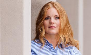 Porträt von Maxi Müller, angehende MBA-Absolventin der FH Burgenland, in einem blauen Hemd vor heller Wand – sie spricht im Interview über Fernstudium, Motivation und Zeitmanagement.