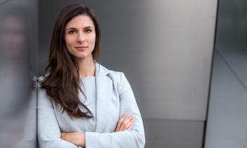 LL.M. Wirtschaftsrecht an der Hochschule Burgenland Junge Frau im hellen Blazer steht mit verschränkten Armen vor einer modernen Metallfassade und blickt selbstbewusst in die Kamera – Symbol für praxisorientiertes Fernstudium im Wirtschaftsrecht an der Hochschule Burgenland.
