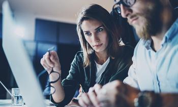 Zwei konzentriert wirkende Personen im Business-Outfit besprechen Unterlagen vor einem Laptop in einem modernen Büro – Symbolbild für den MBA-Lehrgang Compliance & Risikomanagement.