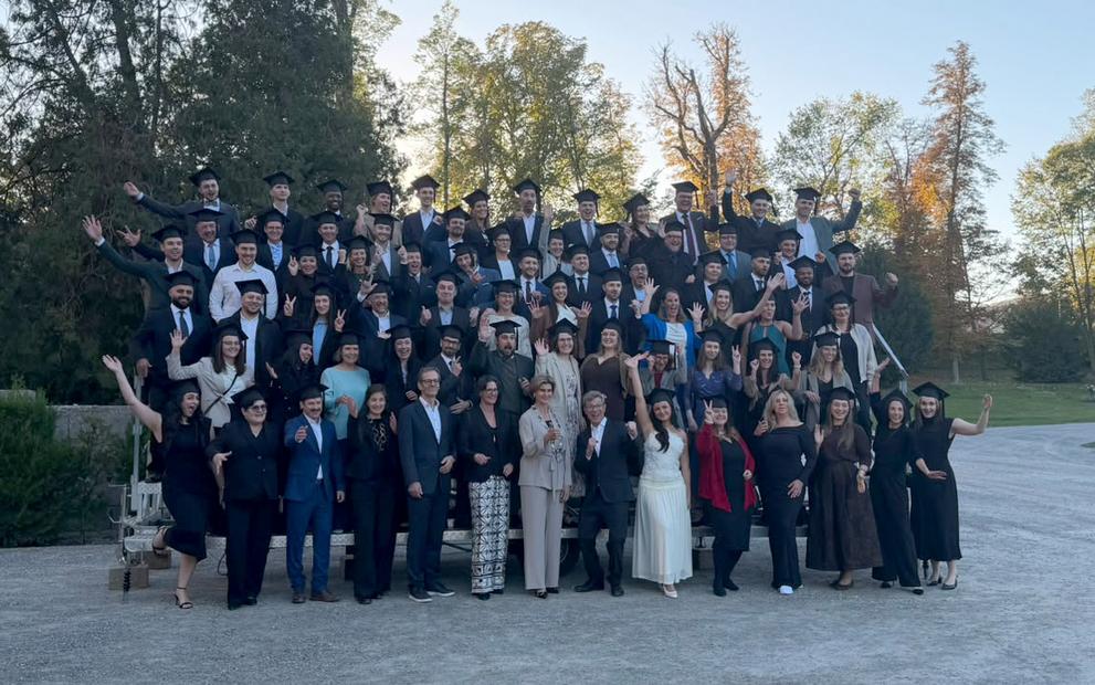 Absolventen einer Universität in Österreich posieren in Talaren und mit Abschlusskappen für ein Gruppenfoto.