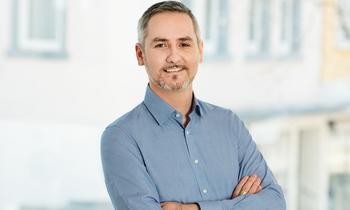 Marcel S., MBA-Student an der FH Burgenland, steht mit verschränkten Armen in einem modernen, hellen Innenraum und lächelt in die Kamera.
