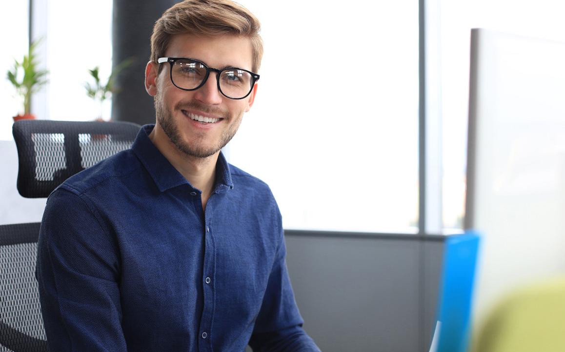 Junger Mann mit Brille im modernen Büro, lächelt selbstbewusst – steht für digitale Kompetenz und strategische Weiterbildung im Bildungsmanagement.