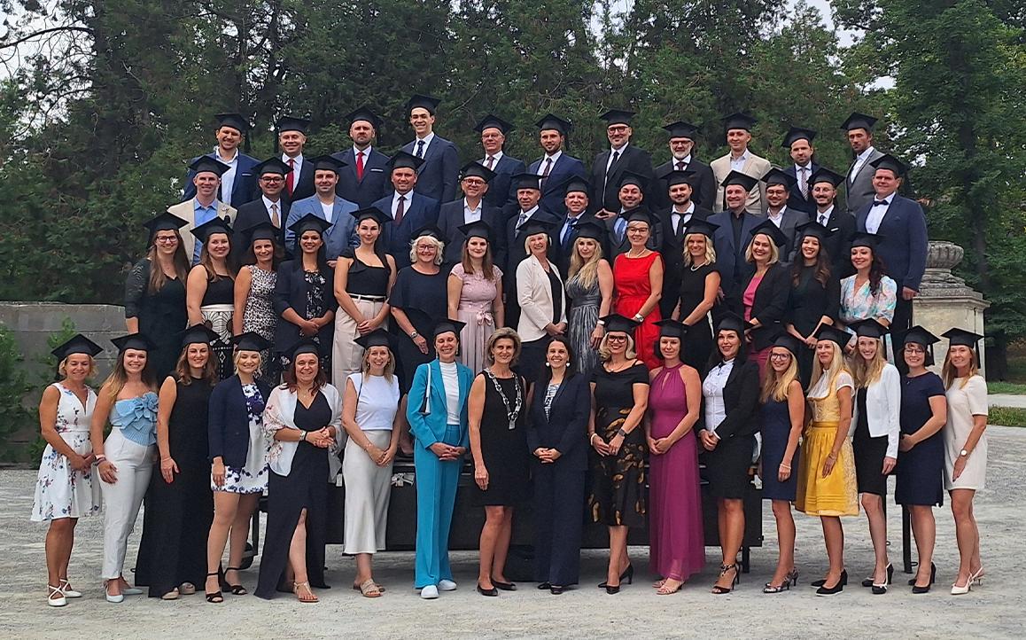 Gruppenfoto von Absolventinnen und Absolventen der FH Burgenland mit Sponsionshüten im Schlossgarten von Schloss Esterházy – feierlicher Moment nach der Sponsion 2024.