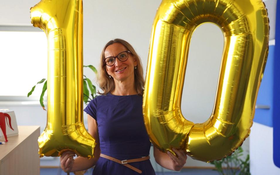 Eine lächelnde Mitarbeiterin der FH Burgenland Weiterbildung hält zwei große goldene Ballons in Form der Zahl 10 – ein festlicher Moment zum 10-jährigen Bestehen der Weiterbildungsprogramme.