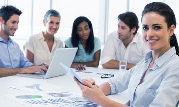 Business-Team in moderner Besprechungssituation – eine Frau im Vordergrund mit Tablet, symbolisiert praxisnahe Führungsweiterbildung im MBA Business Management der FH Burgenland.
