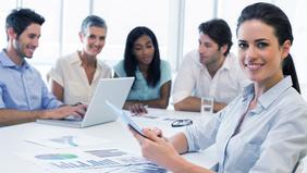 Business-Team in moderner Besprechungssituation – eine Frau im Vordergrund mit Tablet, symbolisiert praxisnahe Führungsweiterbildung im MBA Business Management der FH Burgenland.