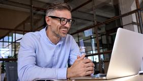 Lächelnder Mann mit Brille und hellem Hemd arbeitet konzentriert an einem Laptop – Sinnbild für flexibles Online-Studium im Bereich digitale Geschäftsmodelle an der Hochschule Burgenland.