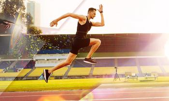 MSc (CE) Sportphysiotherapie Sportlicher Mann im schwarzen Outfit sprintet über eine Laufbahn in einem Stadion bei Sonnenlicht. Im Hintergrund sind Tribünen und Kameraequipment sichtbar – symbolisch für das praxisorientierte MSc-Programm Sportphysiotherapie der FH Burgenland.