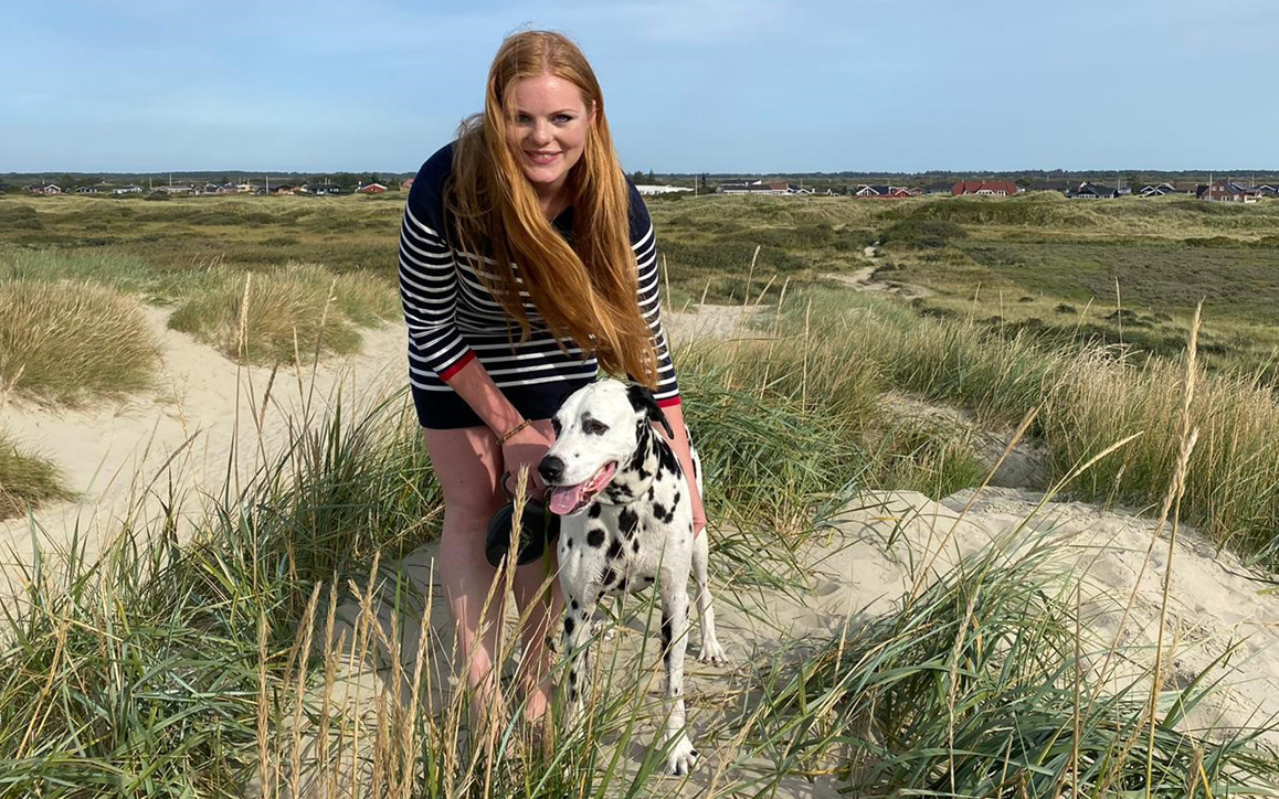 Maxi Müller mit ihrem Dalmatiner „Kiwi“ in den Dünen am Meer. Sie kniet lachend neben ihrem Hund – ein privater Einblick in ihre Freizeit und den sportlichen Ausgleich zum Studium.