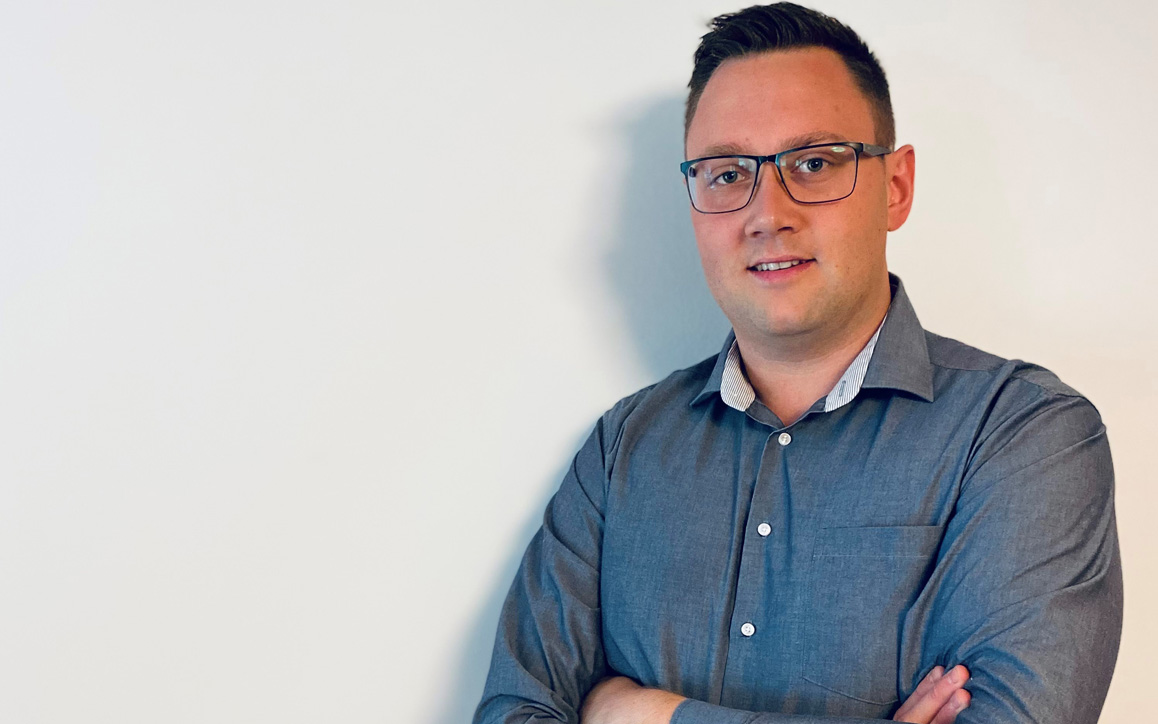 Michael Prodinger steht mit verschränkten Armen vor einer hellen Wand und blickt selbstbewusst in die Kamera. 