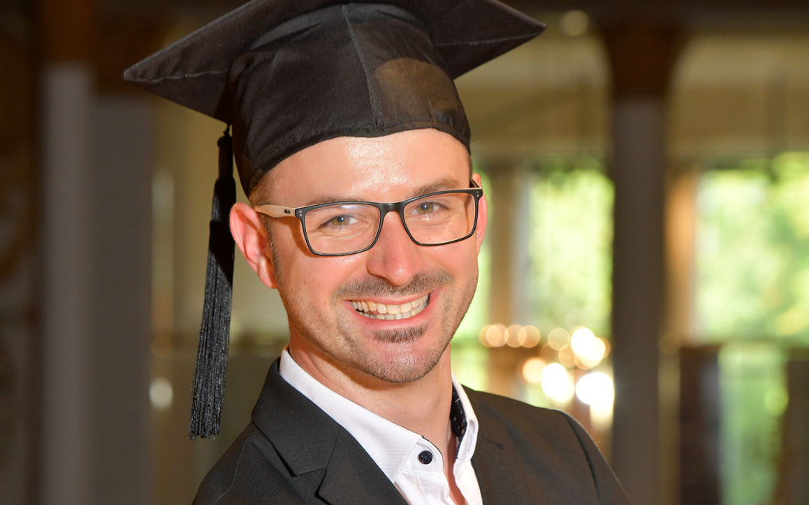 Arno Kersche mit Abschlusskappe und Brille, lachend in festlicher Umgebung – Symbol für seinen erfolgreichen MBA-Abschluss an der FH Burgenland.