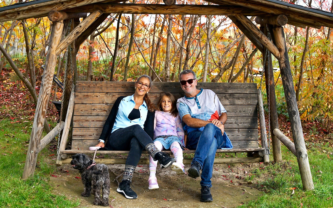 Elke Egi mit ihrem Partner, Kind und Hund auf einer Holzschaukel in einem herbstlichen Garten – Familienzeit und Natur als Ausgleich zum Studium.