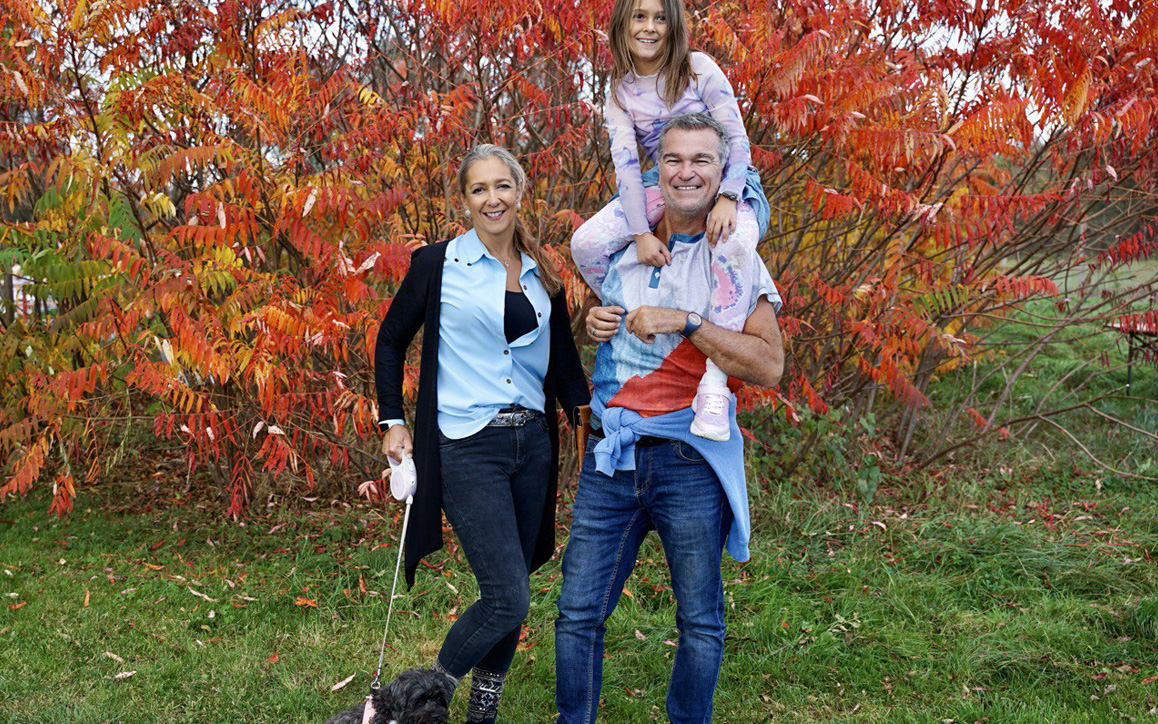 lke Egi mit ihrer Familie vor einer farbenfrohen Herbstkulisse – sie hält den Hund an der Leine, ihr Partner trägt die Tochter auf den Schultern – ein Bild für Zusammenhalt und Lebensfreude.