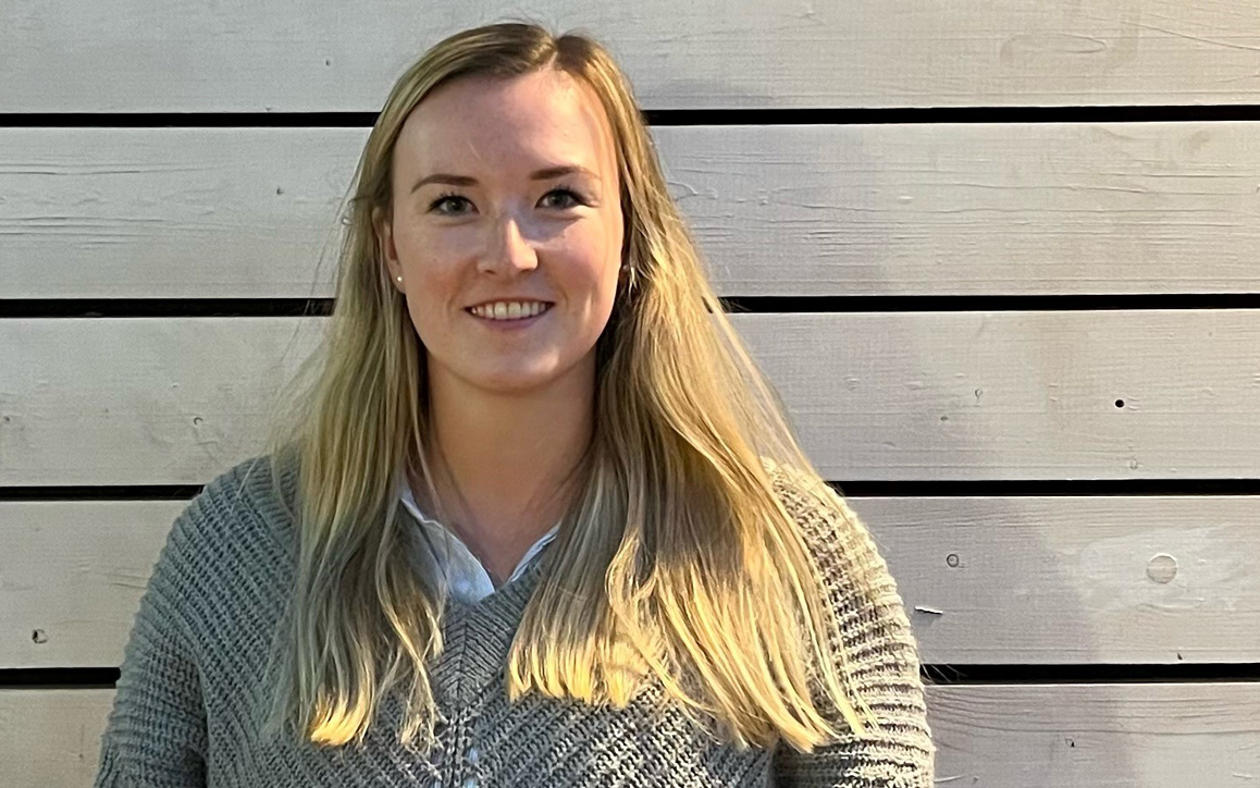 Alexandra van Bracht, MBA-Studierende der FH Burgenland, mit blondem Haar und grauem Strickpullover, lächelt in die Kamera. 