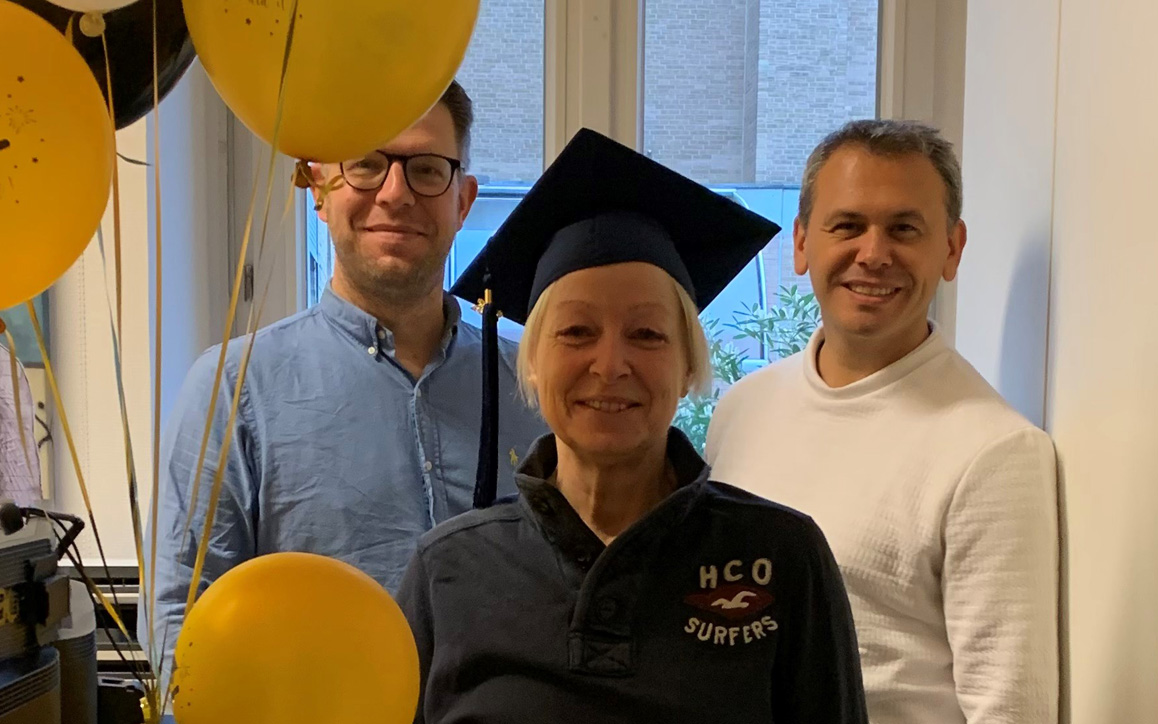 Birgit Giese mit Graduation Cap feiert mit Kolleg*innen, umgeben von gelben Ballons und Konfetti.