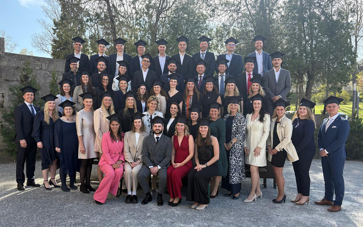 Gruppe von Absolvent*innen mit Sponsionshüten lächelt in die Kamera im Schlossgarten von Schloss Esterházy.