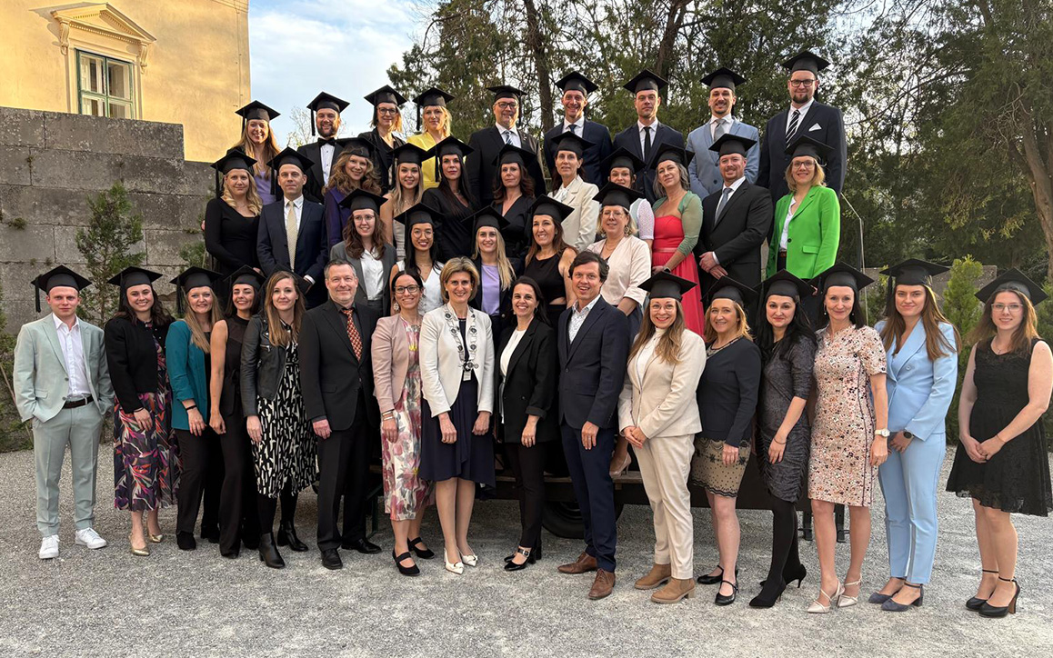 Mehrere Absolvent*innen mit Hut versammeln sich lachend zu einem Gruppenfoto im Schlosspark von Esterházy.