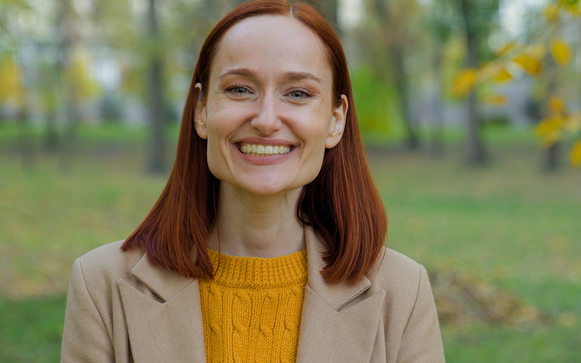 Akademische Weiterbildung mit Zertifikat Junge Frau lächelt in die Kamera, im Hintergrund herbstlicher Park. Sie steht für akademische Weiterbildung mit Zertifikat an der Hochschule Burgenland.