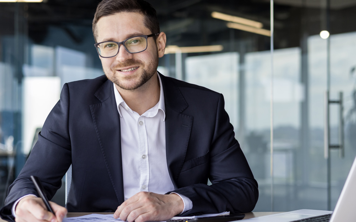 Freundlich lächelnder Mann am Laptop – steht für Kompetenz, digitale Weiterbildung und die neuen ERP-Programme der Hochschule Burgenland.