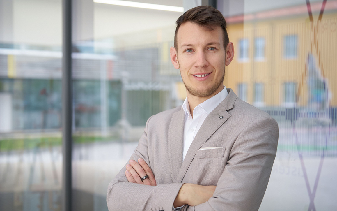 Porträt von Christoph Tatzber im Anzug, aufgenommen im Freien. Im Hintergrund ist ein helles Gebäude erkennbar – Symbolbild für beruflichen Erfolg und persönliche Weiterentwicklung.
