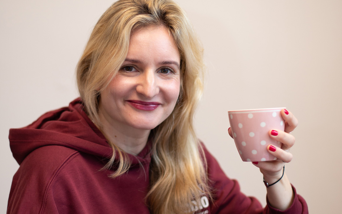 Franziska Gattringer blickt lächelnd in die Kamera und hält eine Kaffeetasse in der Hand.